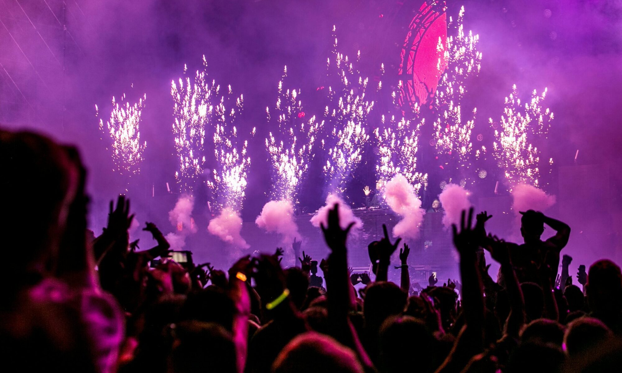 Vibrant EDM concert scene with fireworks, smoke, and enthusiastic crowd enjoying the music.