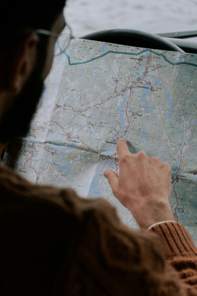 Close-up of a person's hand pointing at a map inside a car, emphasizing travel.